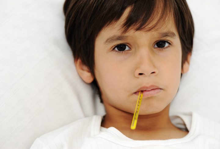 Sick little boy with thermometer, laying on bed